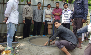 A group of men stands around a concrete tube well being constructed by a mason.