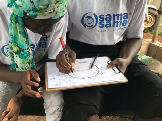 Two members of the Sama Sama team are writing out their thoughts on the Day in the Life tool while sitting on a bench during the DISCOVER phase of this HCD work.