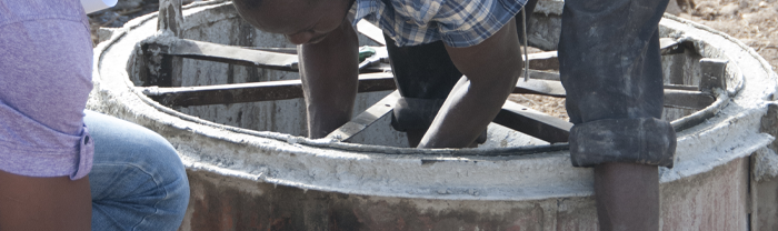 A latrine business owner positions a circular metal mold inside of a concrete latrine pit ring.